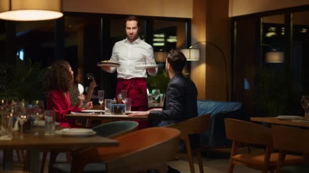 Waiter serving hungry couple in fancy restaurant. Man putting plates on table. — Stock Video