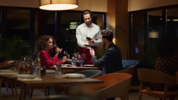 Gece randevusunda restoran faturasını ödeyen çift. Garson kafede müşterilere servis yapıyor.. — Stok video