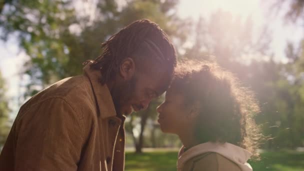 Cute child touching forehead smiling father in golden sunlight park portrait. — Stock Video