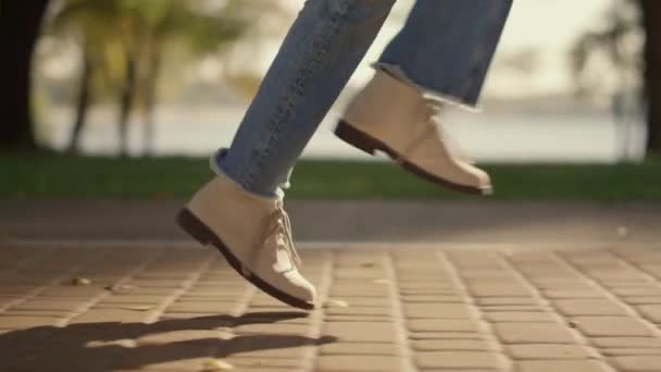 Neşeli kız bacakları yürüyor güneşli levhalarla kaplı yol parkında arkasında gölgeler bırakarak. — Stok video