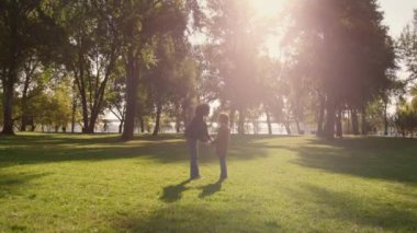 Annesinin elini tutan kız altın güneş ışığında parkı gözetliyor..