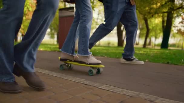Pernas de menina andando de skate no parque close-up. Pais desconhecidos apoiam criança. — Vídeo de Stock
