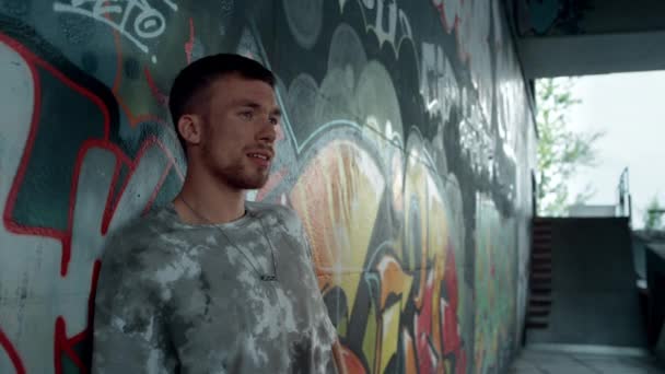 Young hipster relaxing near wall with graffiti. Calm millennial looking away. — Stock Video