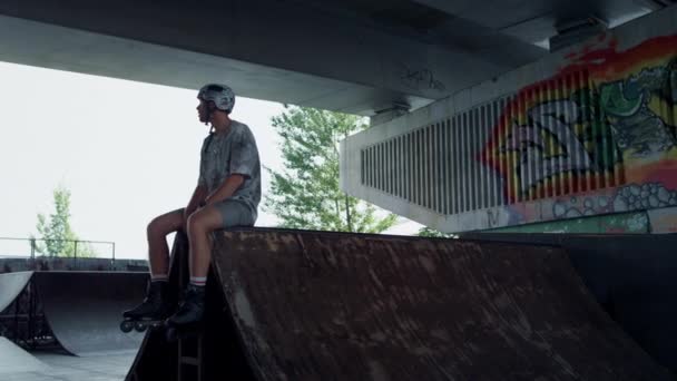 Uvolněný bruslař odpočívající na rampě v skateparku. Pohledný muž má pauzu — Stock video