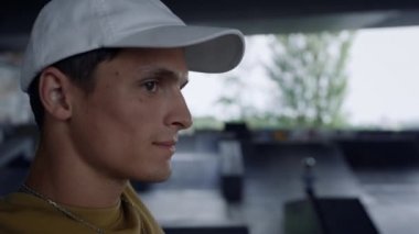 Gülen adam kaykay parkında antrenman yapıyor. Yan gözle bakan adam ileriye bakıyor.. 