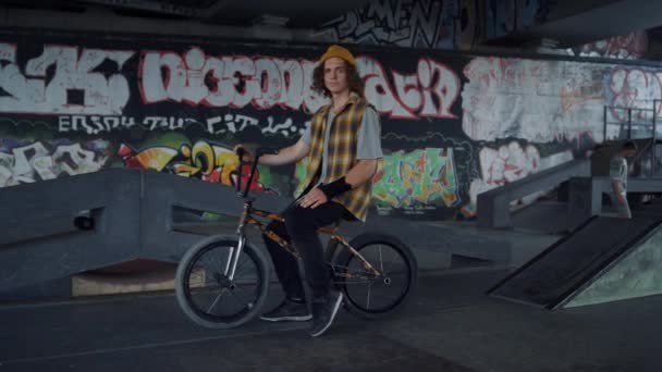 Pozytywny mężczyzna po przerwie po treningu na rowerze bmx w skate parku graffiti. — Wideo stockowe
