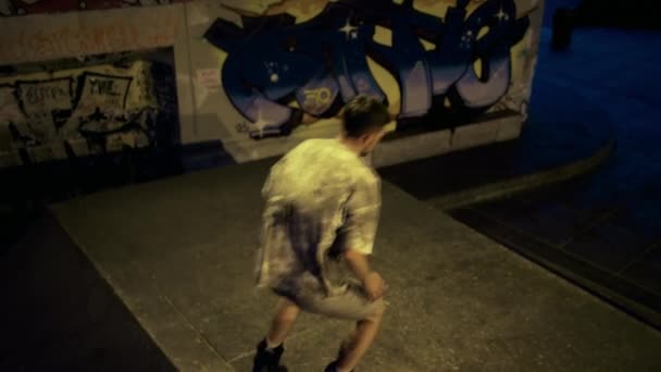 Teenage jezdci trénink společně v skateparku s graffiti zeď ve večerních hodinách. — Stock video