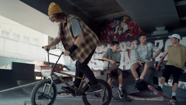 Aktywny mężczyzna ćwiczący rower bmx w skate parku z graffiti na ścianie. — Wideo stockowe