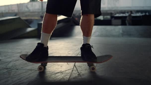 Mladý bruslař provádějící skok trik na skateboardu v skate parku. Nohy v teniskách — Stock video