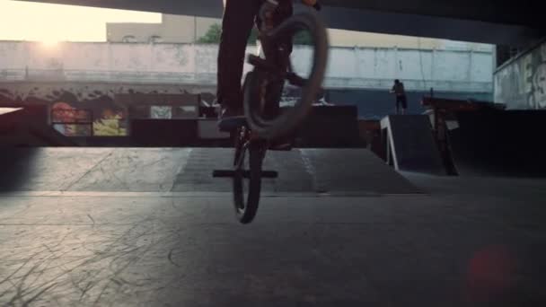 Tiener bmx rijder het uitvoeren van jump stunt op felle zon achtergrond in skate park. — Stockvideo