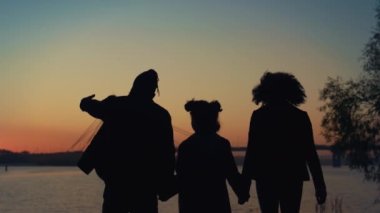 Aile silueti el ele tutuşuyor. Gün batımı manzaralı nehir kıyısına gidiyorlar..