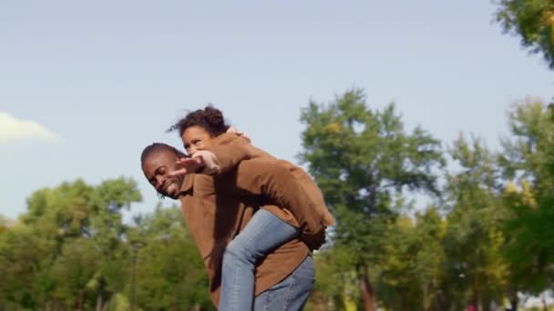 Joyeux papa piggyback enfant dans un parc ensoleillé. Lien émotionnel enfance insouciante. — Video