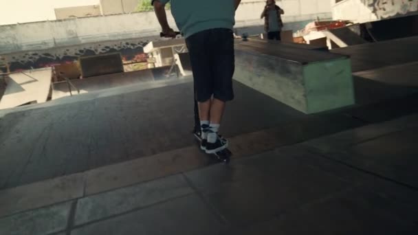 Aktivní chlapec skákání triky na skútru v skateparku. Jezdec převrací na skútru. — Stock video