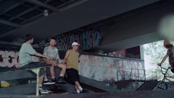 Adolescentes activos viendo entrenamiento en bicicleta bmx en skate park con graffiti. — Vídeo de stock