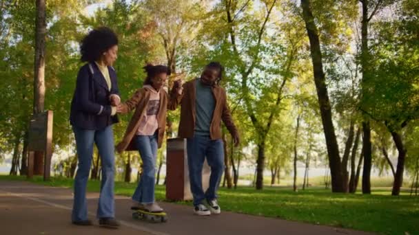 Rodiče učí dívku jezdit na longboardu v parku. Podpůrná rodina povzbuzuje dítě. — Stock video