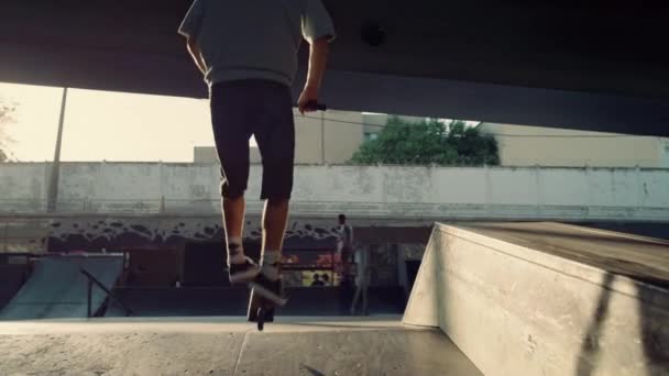 Αθλητικοί άνδρες jumping κόλπα για σκούτερ και bmx ποδήλατο στο αστικό πάρκο skate. — Αρχείο Βίντεο