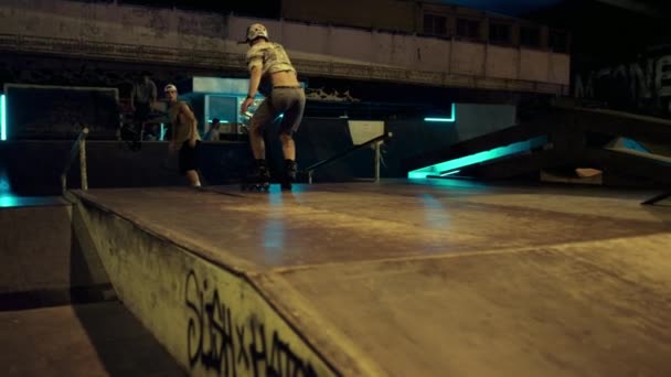 Активные хипстеры выполняют прыжок на трамплине в ночном скейт-парке с граффити. — стоковое видео