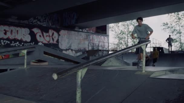 Millennial człowiek skacze na szynie z hulajnoga w miejskim skate parku. — Wideo stockowe