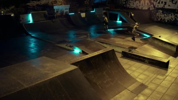 Юные спортсмены вместе выполняют трюк в скейт-парке со стеной для граффити. — стоковое видео