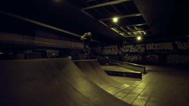 Sportif adam gece kaykay parkında BMX bisikleti üzerinde tehlikeli bir numara yapıyor.. 