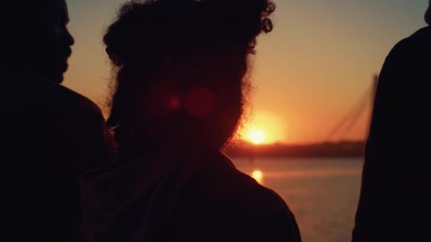 Krullend meisje silhouet staan met ouders bij gouden zonsondergang achteraanzicht closeup. — Stockvideo