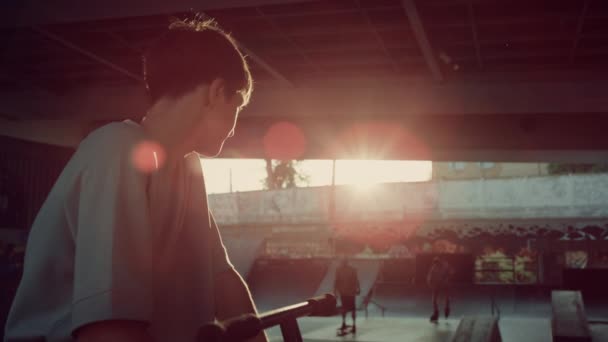 Молодой человек отдыхает после тренировки в скейтпарке. Человек смотрит в камеру. — стоковое видео