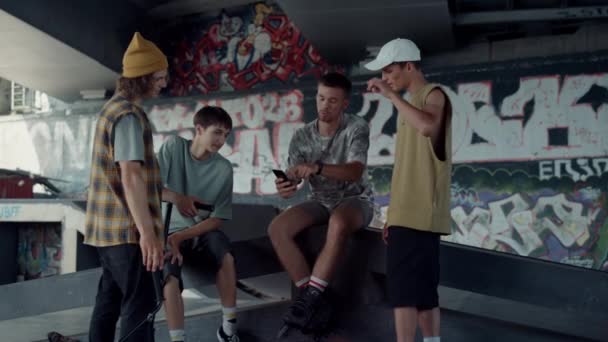 Amigos alegres assistindo vídeo no celular no parque de skate com graffiti. — Vídeo de Stock