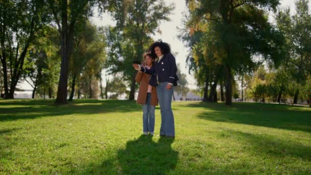 Sonriente mamá haciendo llamadas en línea saludando a la cámara. Familia feliz posando en el parque. — Vídeo de stock