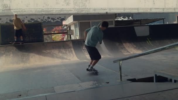 Teenageři přátelé cvičení společně na skútru a skate board v skateparku — Stock video