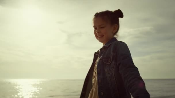 Sahil tatilinde çocukluğunun tadını çıkaran sevimli bir kız. Çocuk deniz kıyısında dans ediyor.. — Stok video