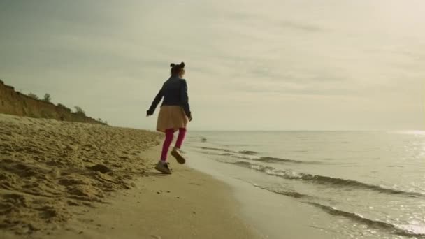 Dziewczynka bawiąca się na plaży w morskiej naturze. Wesoły dzieciak skaczący po piaskowej linii brzegowej. — Wideo stockowe