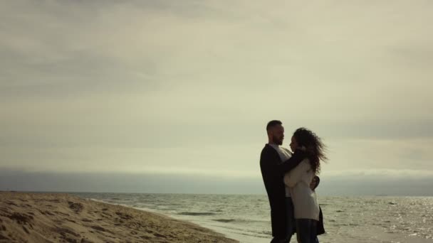 Пара, що стоїть на морському пляжі в повсякденному одязі. Закохані обіймаються у відпустку . — стокове відео