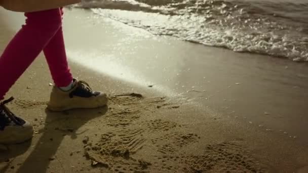 小女孩的腿在沙滩上走着。孩子的脚走了，波涛汹涌 — 图库视频影像