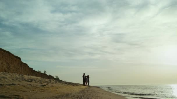 İnsanlar ayakta duran plaj manzarası grubu. Aile gün batımında yürür dalgalar çarpar. — Stok video