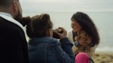 Deniz sahilinde fotoğraf makinesi oynayan bir aile. Oyuncak ayının fotoğrafını çeken ebeveyn çocuğu.