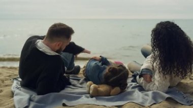 Anne ve babası deniz kıyısında plajda yatıyor. Mutlu aile piknikte oynuyor..