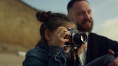 Elinde kamera olan küçük bir çocuk deniz kıyısı manzaralı aile gezisinin fotoğraflarını çekiyor..