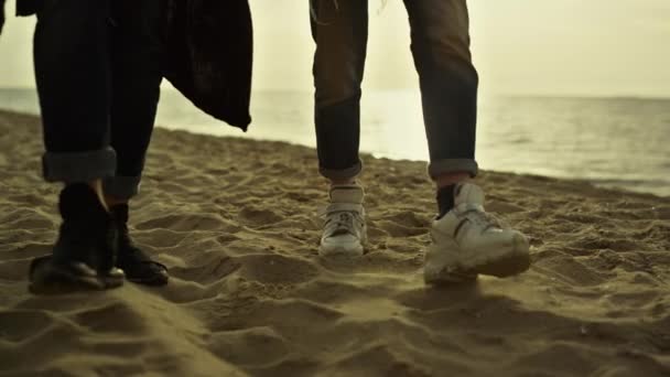 日落时分，人们的腿在沙滩上散步。两只手踩到岸上. — 图库视频影像