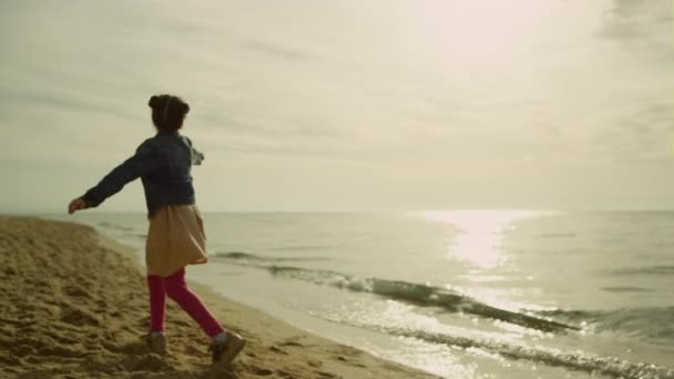 Malá dětská tančící pláž při západu slunce. Šťastná dívka hraje sama venku. — Stock video