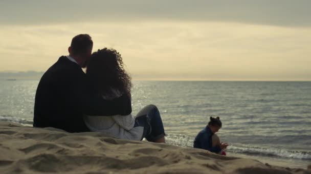 松懈的人们欣赏日落海滩.一家人坐在沙滩上感到冷. — 图库视频影像