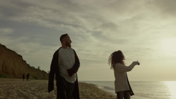Giocoso coppia a piedi spiaggia tramonto mare cielo. Gli amanti amano tenersi per mano sulla costa. — Video Stock