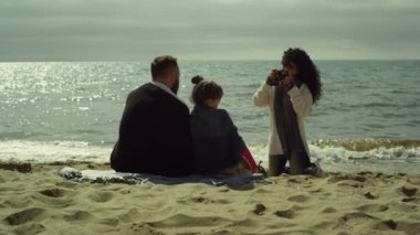 Genç bir aile güneşli bir plajda fotoğraf çekiyor. Anne baba, çocuk deniz fotoğrafı çekiyor.