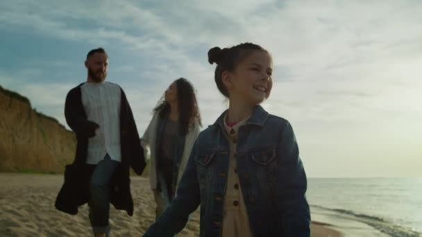 Γονείς κορίτσι με τα πόδια ακτή από την ανατολή κύματα της θάλασσας. Οικογένεια απολαμβάνουν ωκεανό διακοπές στην παραλία. — Αρχείο Βίντεο