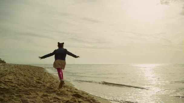 Κορίτσι τρέχει άμμο θάλασσα στο ηλιοβασίλεμα. Μικρό παιδί εξερευνήσετε άδεια παραλία την ηλιόλουστη μέρα. — Αρχείο Βίντεο