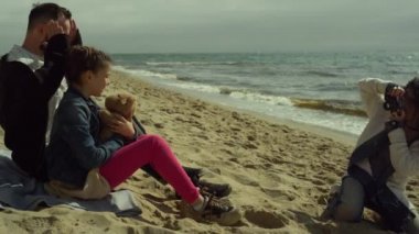 Okyanus kumsalında fotoğraf çeken neşeli bir aile. İnsanlar kumda birlikte rahatlar.. 