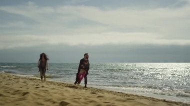 Anne ve babası deniz kenarında kumsalda oynuyorlar. Neşeli insanlar doğada eğleniyor..