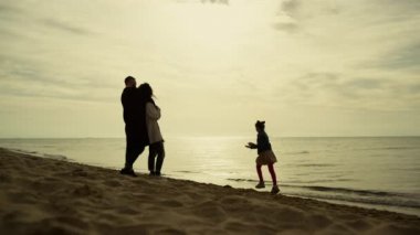 Aile plaj tatili. Ebeveynler sabah deniz kıyısında oynayan çocuğa bakıyorlar.