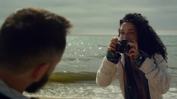 Kvinna tar familjefoton vid havet vågor stranden. Lockigt hår flicka med kamera. — Stockvideo
