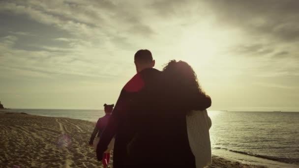 Güzel bir aile okyanus sahilinde gün batımına bakıyor. Anne baba çocuk güzel sahillerde yürüyor.. — Stok video