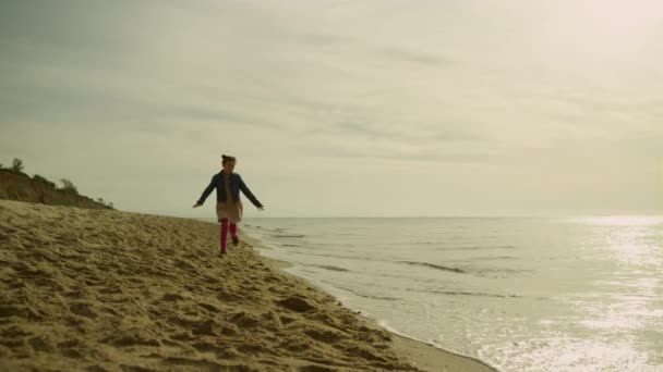 Söt unge som springer i land på morgonen. Lekfull flicka som går iväg strandvågor. — Stockvideo